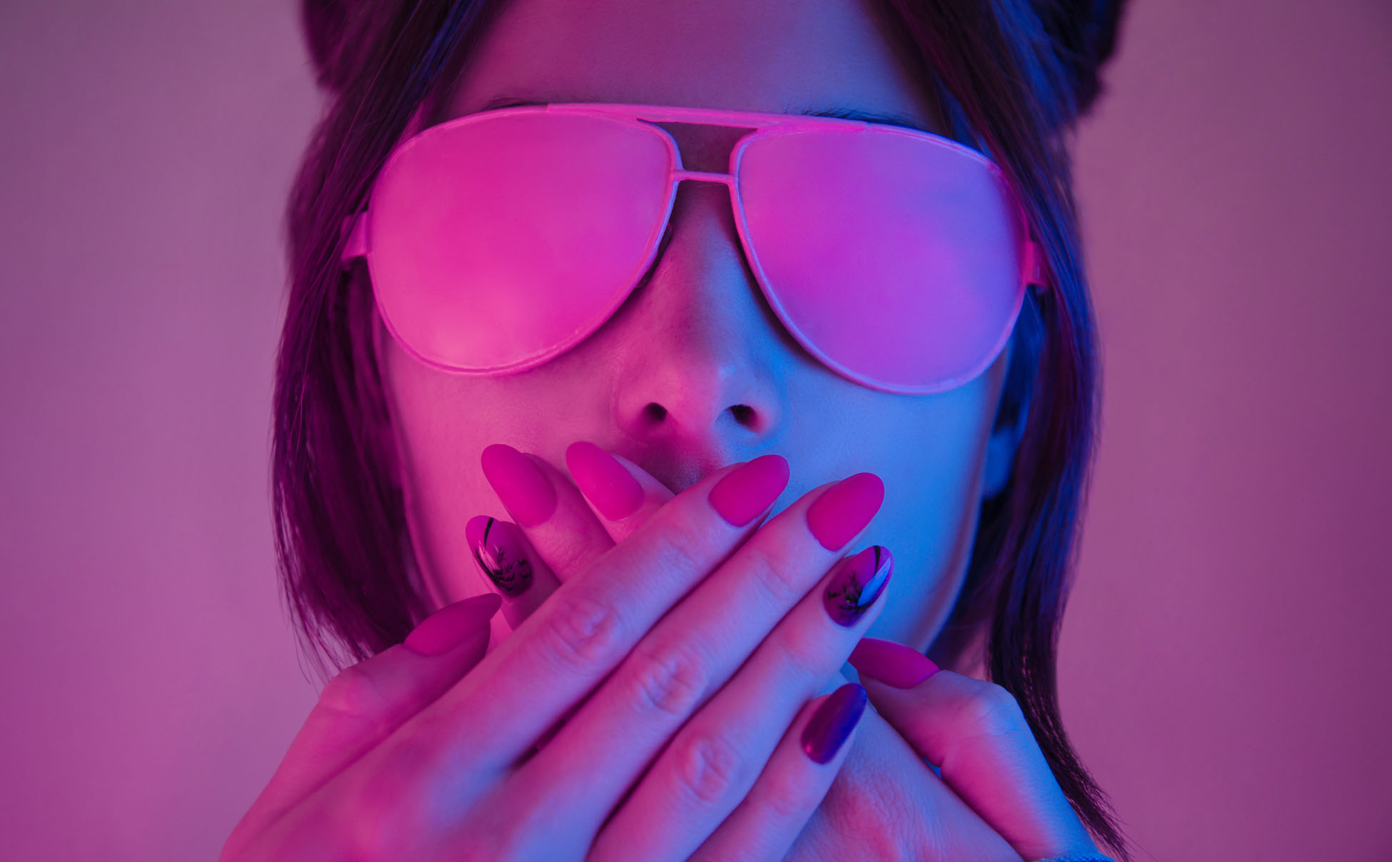 Young woman in pink glasses covers her mouth with hands with a manicure, retrowave style portrait. Demonstration of a beautiful manicure.